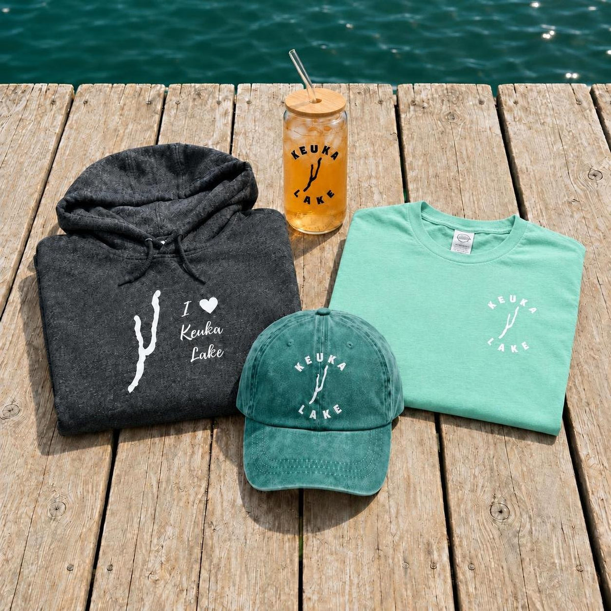 Keuka Lake Merch collection cover: hoodie, tee, cap and can glass on a dock